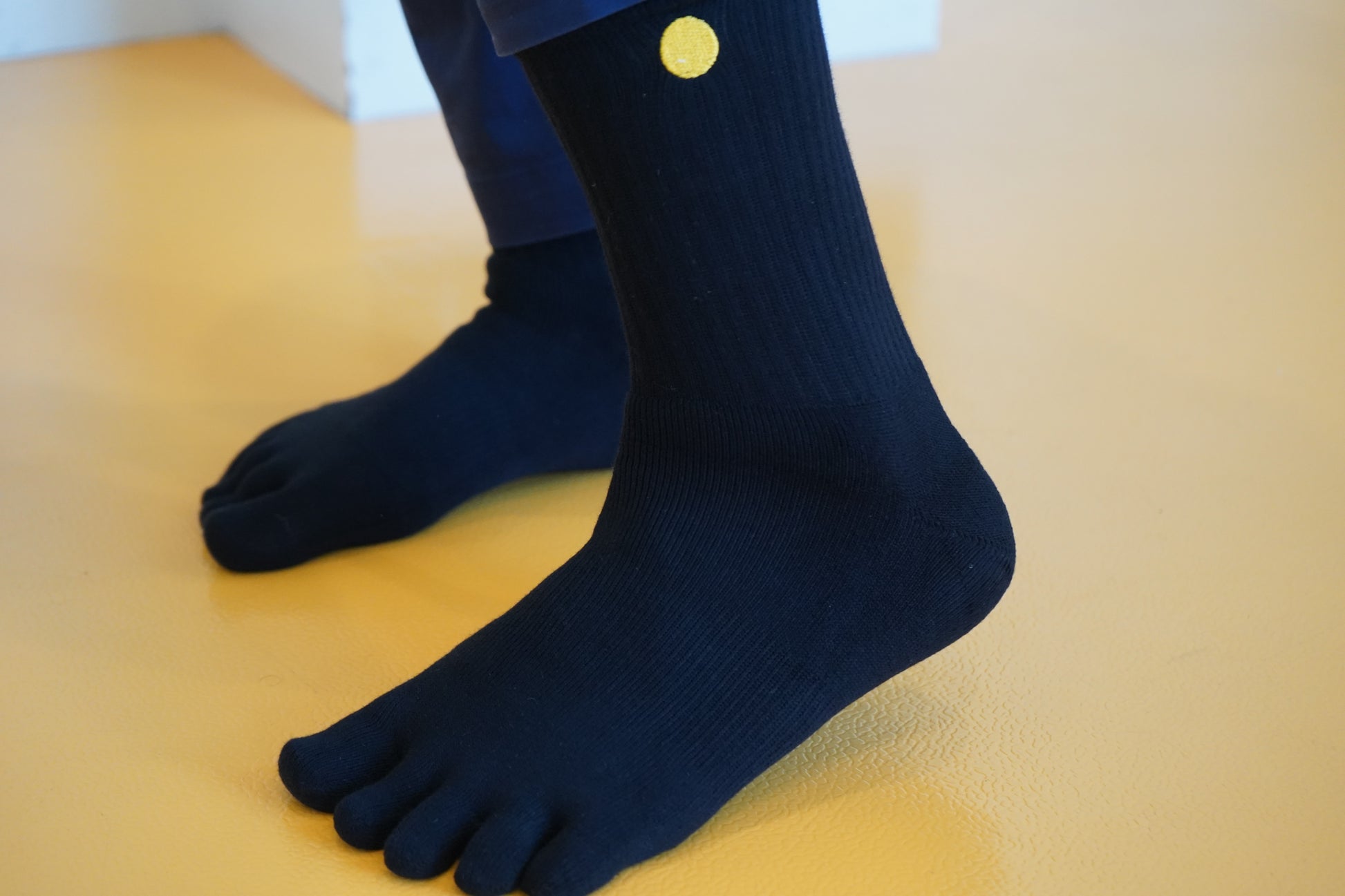 Black five-toe socks with a yellow dot on a yellow floor
