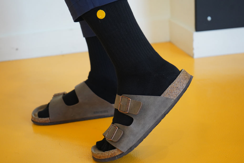 Person wearing brown sandals with buckles on a yellow floor.