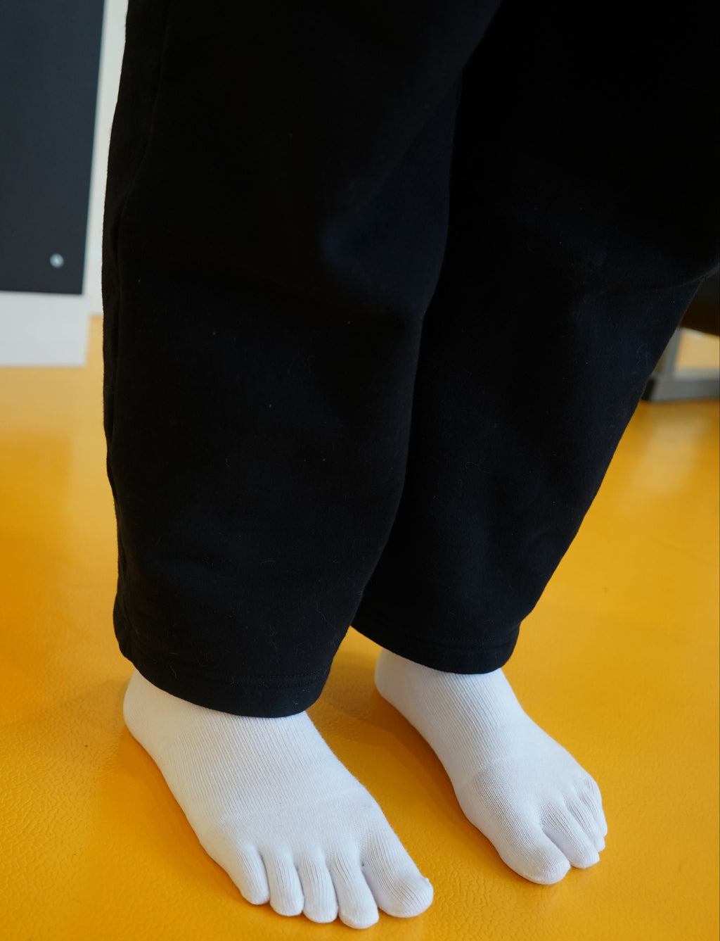 White Toe socks and black pants against a yellow wall.