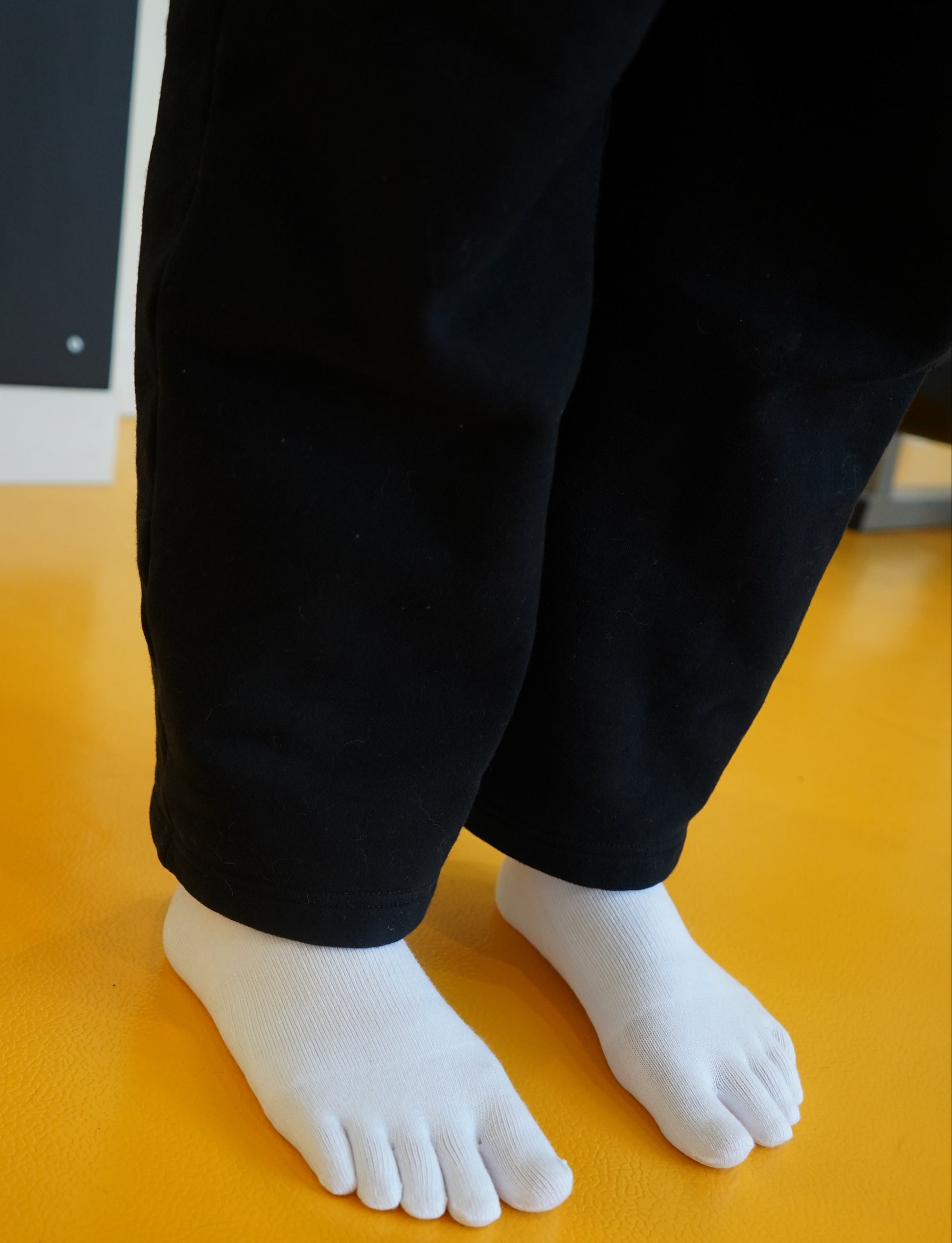 White Toe socks and black pants against a yellow wall.